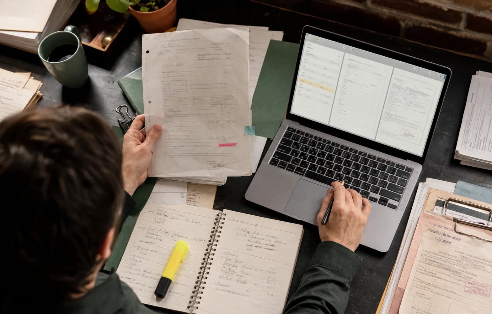 Person prueft Papierdokumente neben einem Dokumenten-Workflow auf einem Laptop